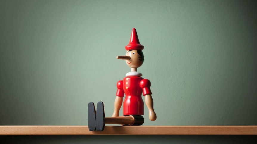 Stock photo of wooden Pinocchio puppet, sitting on a shelf.
