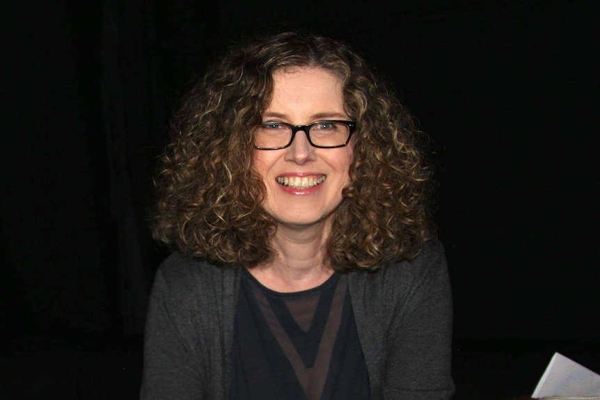 A woman with curly hair sitting holding a mug and smiling