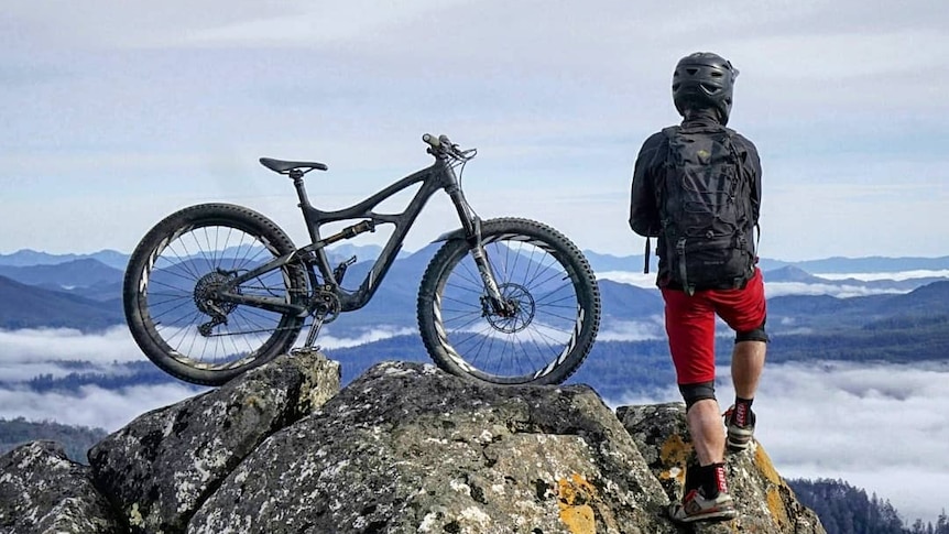 A person stands next to their mountain bike, looking out over hills below.