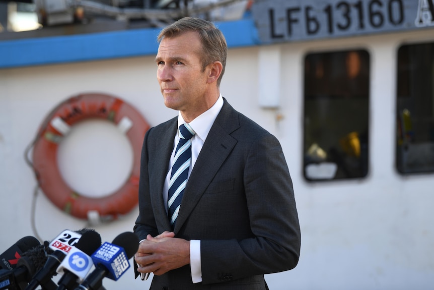 a man wearing a suit standing in front of a tug boat