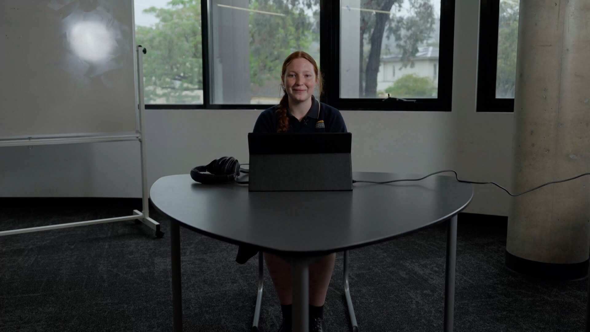 A young woman sits at a desk with a computer. She has her hair tied back.