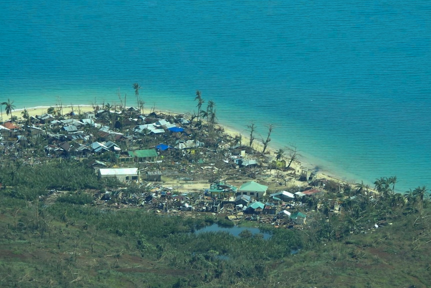 An aerial photo shows damaged homes in a seaside village that is surrounded by lush vegetation and was hit by a typhoon.