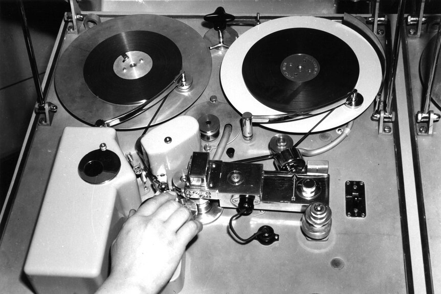 A photo of a hand mixeing audio on an old audio cutting deck.