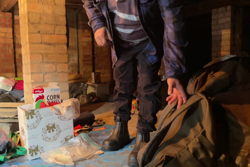 Mężczyzna niosący plecak i inne przedmioty widoczne w słabo oświetlonym pomieszczeniu