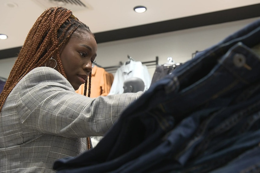 A woman looks at a stack of jeans in a clothing store.