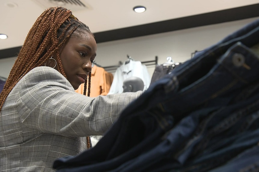 A woman looks at a pile of jeans in a clothing store.