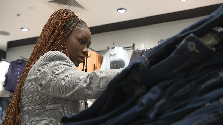 A woman looks at a pile of jeans in a clothing store.