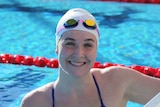 A woman holds onto the blocks at the swimming pool from the water and smiles at the camera.
