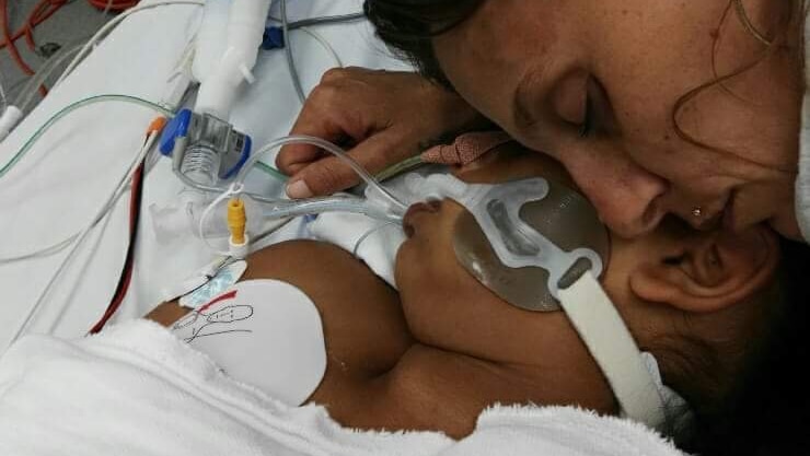 A close up shot of a mother cuddling her girl on a hospital bed.