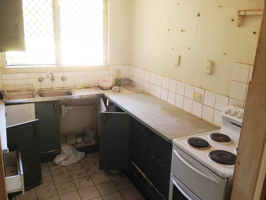 A dirty kitchen with cupboard doors open and rubbish everywhere