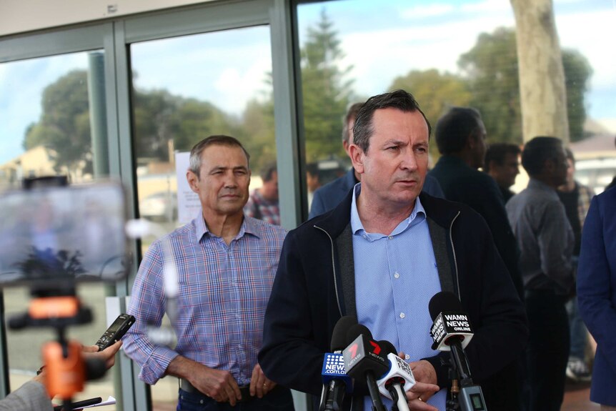 WA Premier Mark McGowan stands before microphones, behind him stands WA Health Minister Roger Cook.