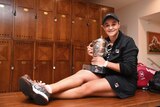 A tennis player sits on a bench in the locker room with the trophy after winning the French Open.