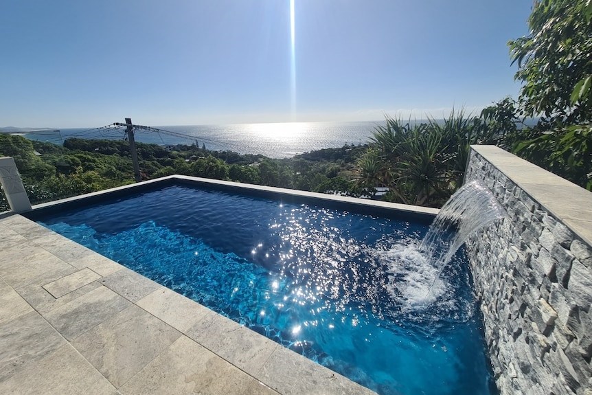 An in-ground pool surrounded by a timber deck with a view of bushland and the ocean