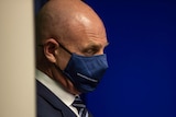 A side-on profile of the Premier wearing a mask in front of a blue background.