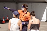 A COVID testing official directs two women at a testing site.