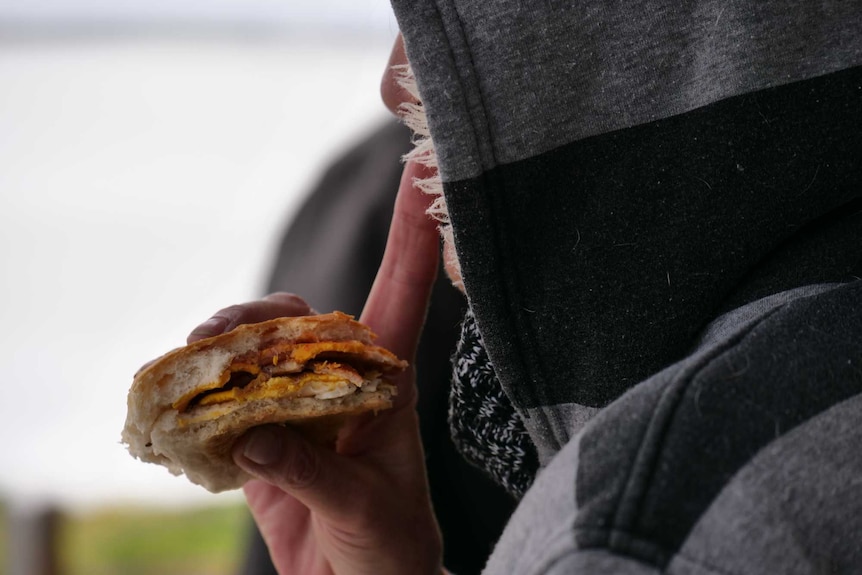 A close up of a egg and bacon roll held up in front of a woman's face. 
