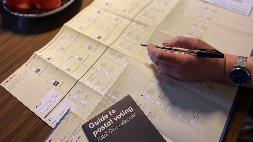 A hand holding a pen about to fill out a ballot paper on a kitchen table.