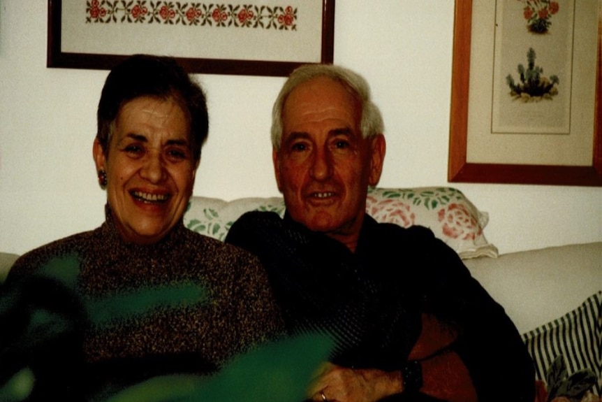 An elderly couple seated on a couch with the woman laughing and the man smiling.