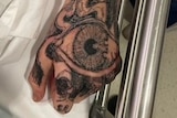 A man's hand with an intricate tattoo of an eyeball that extends across his fingers and up his arm.