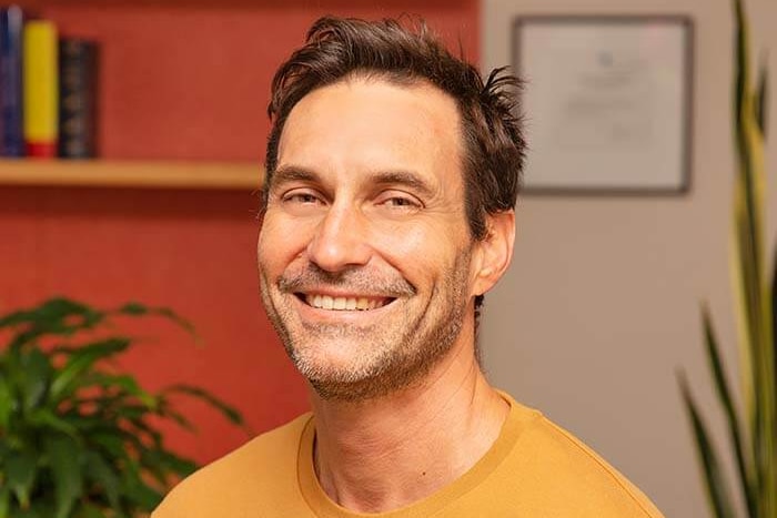 A man in a yellow shirt sits, smiling