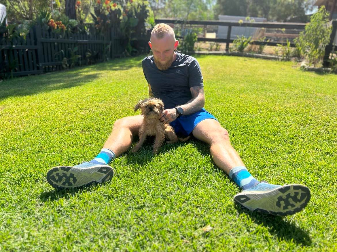 A man sitting down on grass looking at a small dog