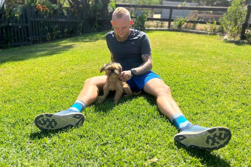 A man sitting down on grass looking at a small dog