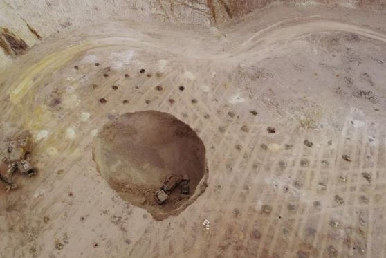 An aerial shot of the sink hole with two mining vehicles sitting at the bottom of it.
