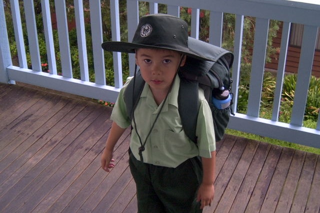 A young boy wearing a school uniform and backpack, on a veranda.
