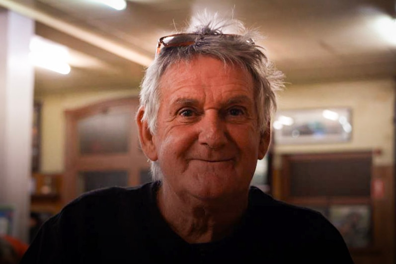 An older man sits in a pub smiling.
