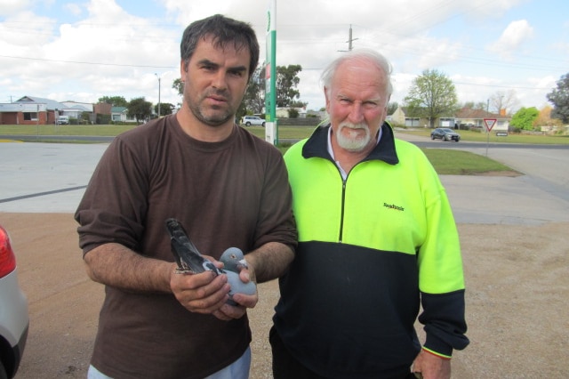 Two men stand side by side, and the younger man on the left holds a pigeon in his two cupped hands.