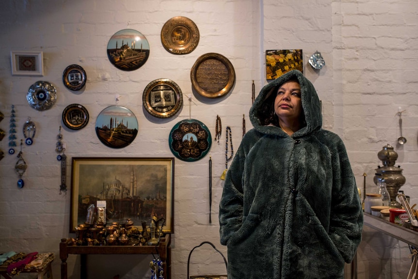 Onur wears a green fake fur hooded coat and stands in front Turkish wall decorations