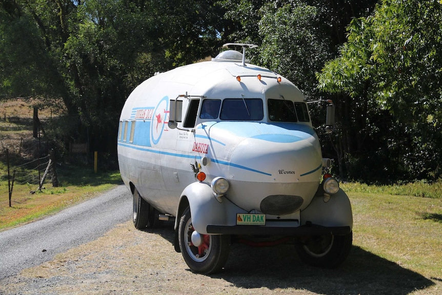 Salvaged DC-3 aircraft wreck turned campervan by the road, in front of some trees