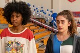 Actors Ayo Edebiri and Rachel Sennott look confused and beat up in a school gym in a still from the film Bottoms.