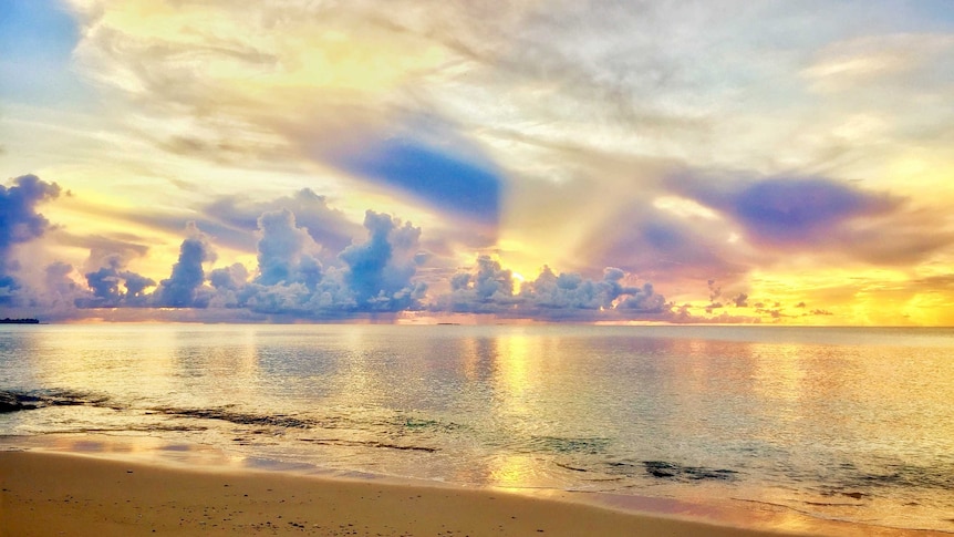 Stunning yellow sunset behind grey clouds over lagoon.