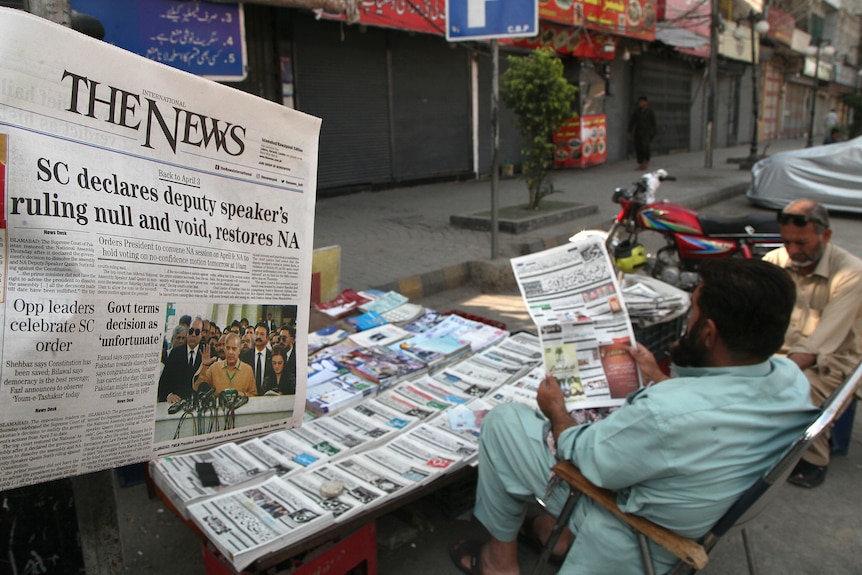 Oamenii citesc copii ale ziarului de dimineață pe o stradă din Pakistan