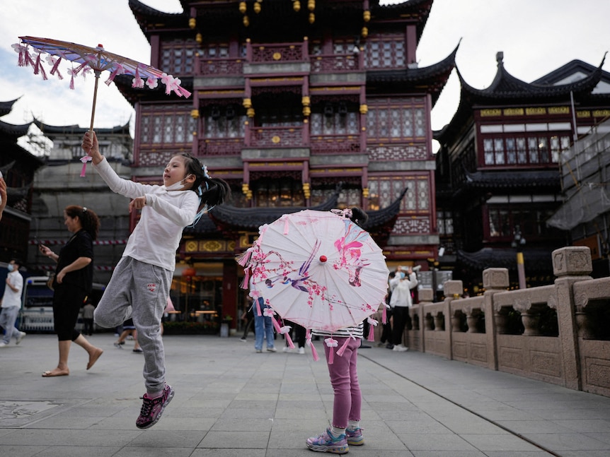 Girls playing with paper umbrellas outside a temple in China