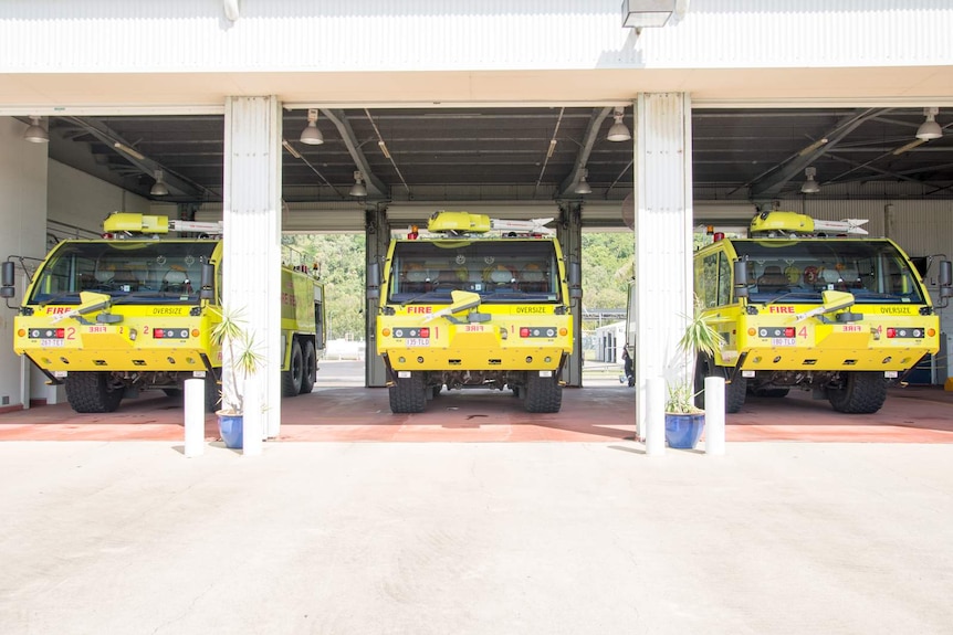 Three bright yellow fire trucks lined up inside the ARFF station garage.