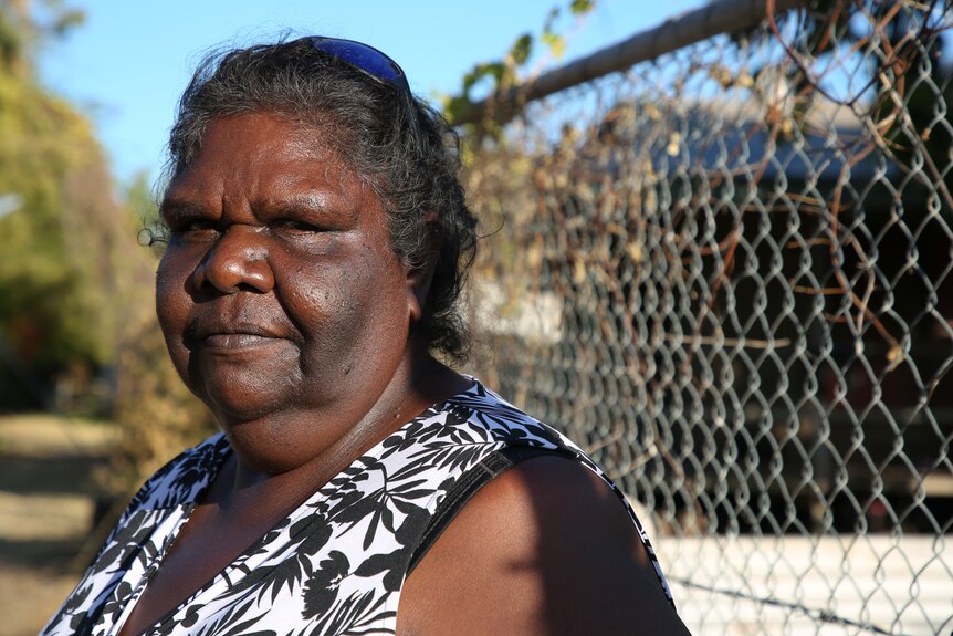 Indigenous leader Lorraine Jones stands in front of a house looking concerned.