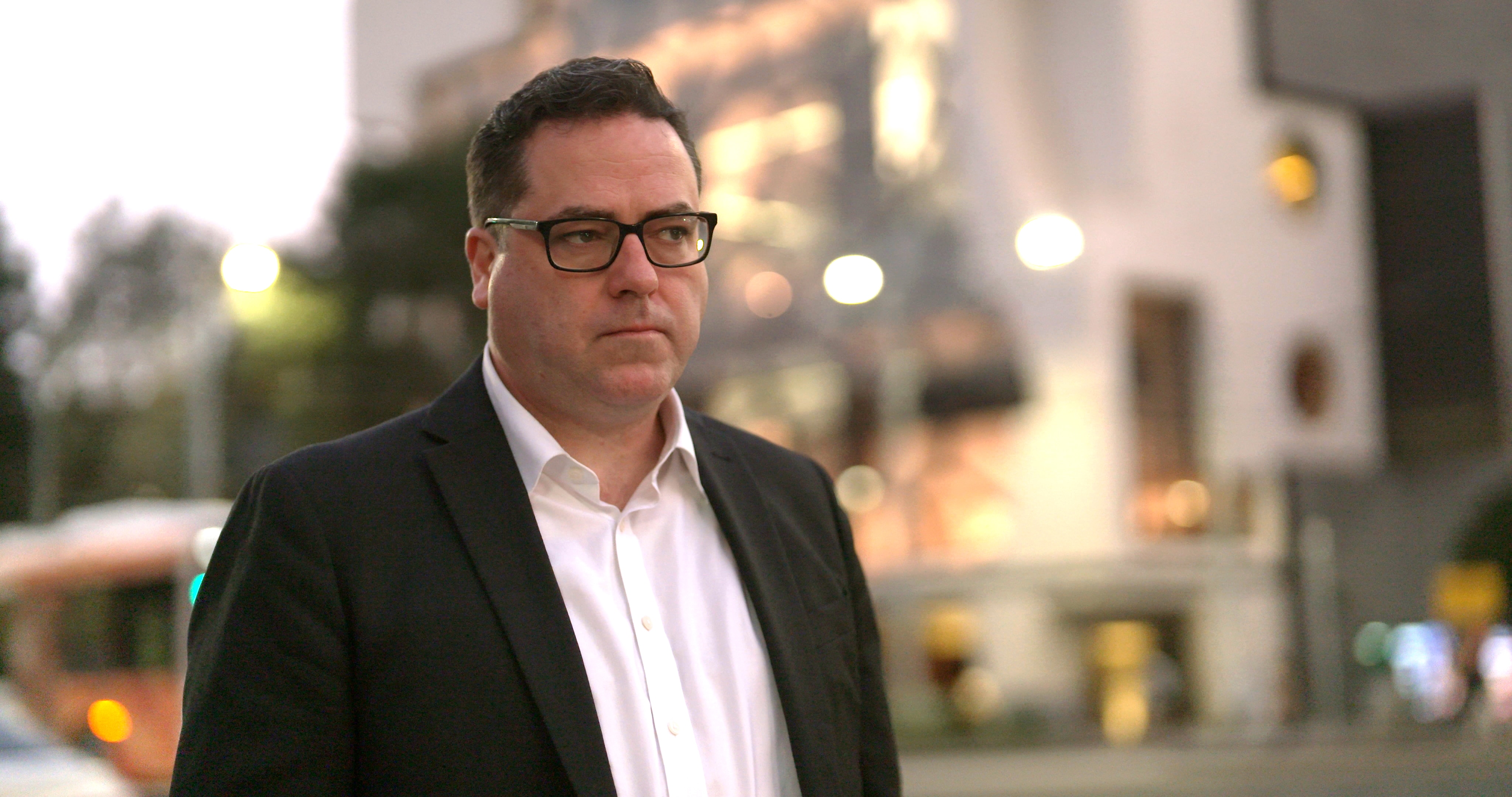 a middle-aged man wearing a white shirt and blazer on a street