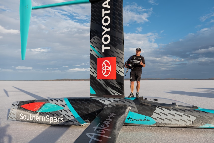 A man standing on a fibreglass aerodynamic vehicle on a salt lake