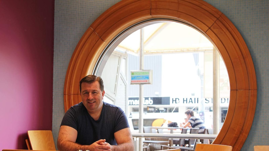 A photo of Sean Johnston in front of a large circular window inside his cafe.