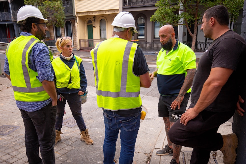 A woman in high vis stands amongst a group of men on a construction site. 
