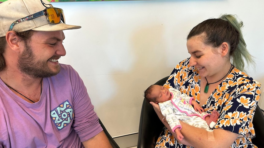 Mum holding her new baby, dad smiling beside them both. 