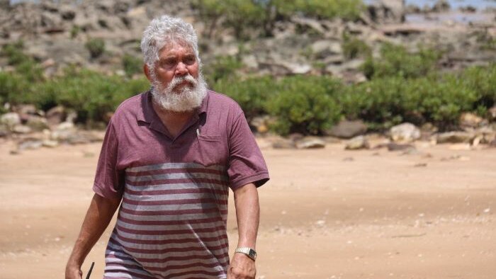 Aboriginal elder Bill Risk walking on a beach.