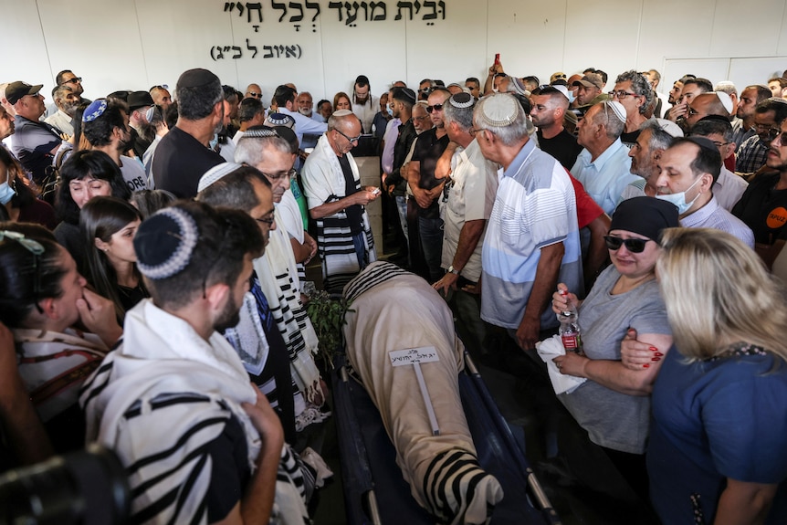 A crowd stands around a wrapped body as it's lowered into the ground. 