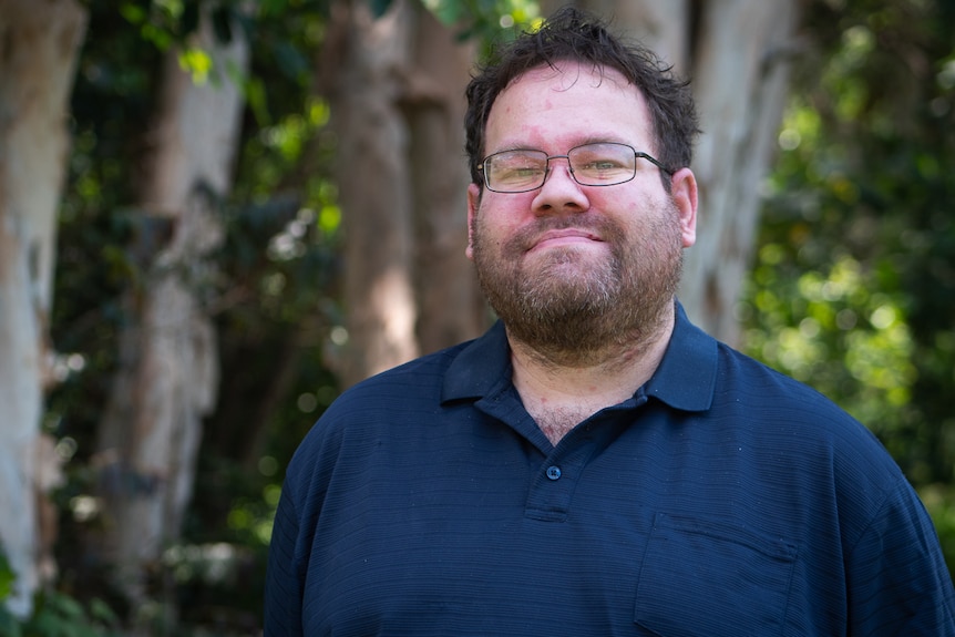 Young Aboriginal man in blue shirt and glasses with trees in the background