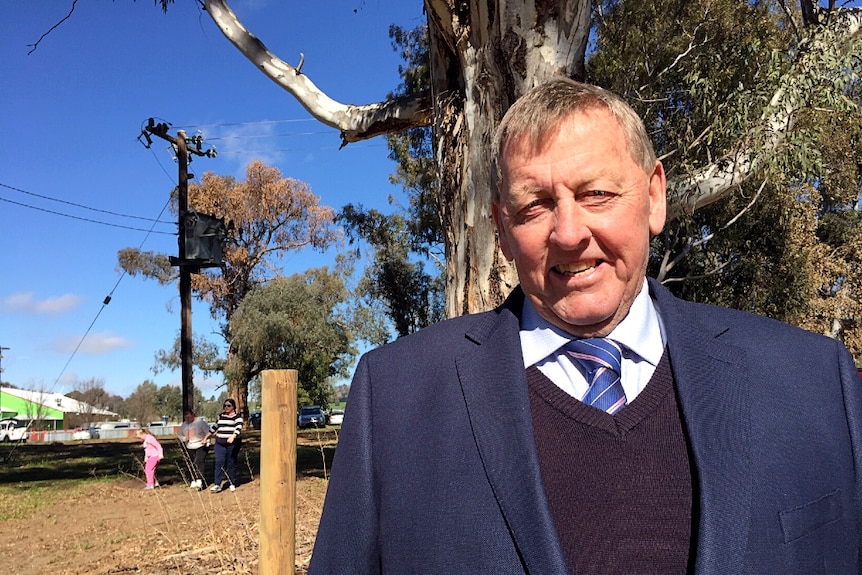 Man standing in front of a large tree, looking at the camera smiling.