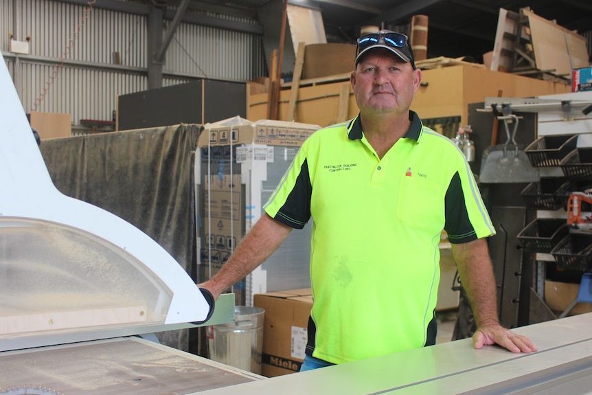 He wears a hi-vis top and stands near a saw