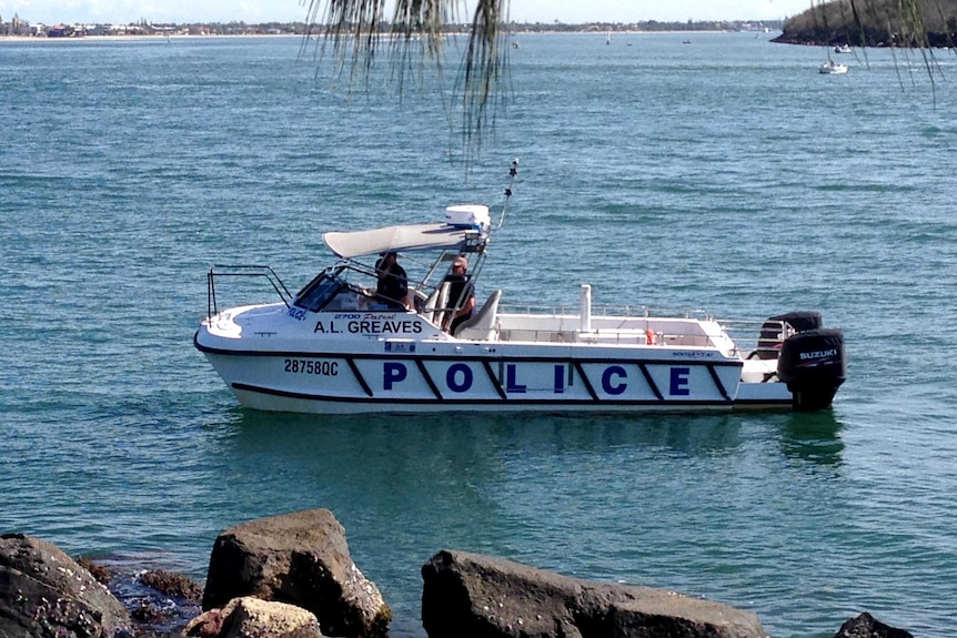 A police boat in the water, with a rocky wall in foreground.