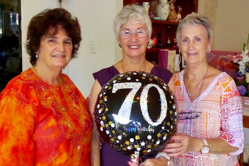 Three women stand for a photo holding a 70th birthday balloon